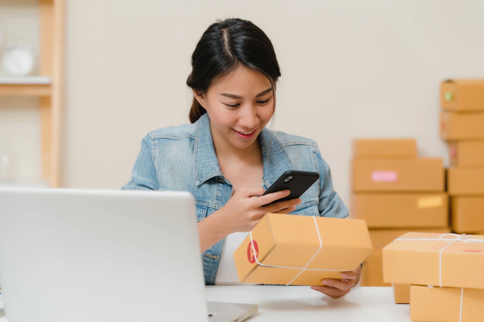 Chủ shop cầm điện thoại kiểm tra đơn bên chồng thùng hàng đã đóng gói